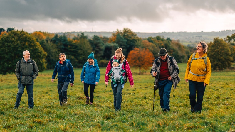 A group of Ramblers of different ages walking across a grassy meadow in winter.